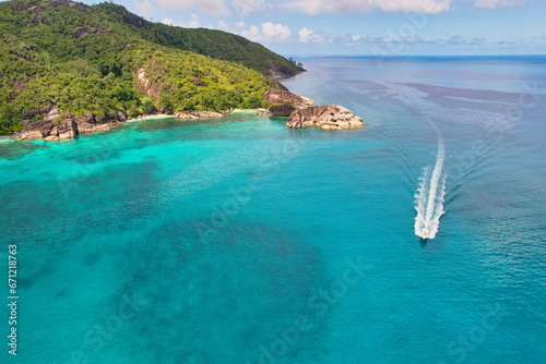 Drone shot of Anse du riz, rice beach beach, transparent sea, lush forest and granite stones, docked and passing boat 1