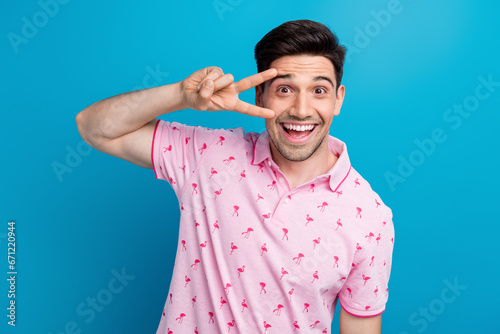 Photo of overjoyed nice person toothy smile arm fingers demonstrate v-sign near eye isolated on blue color background