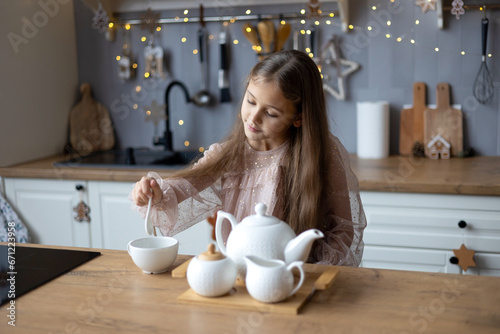 happy cute little girl in beautiful dress preparing tea, christmas morning in the kitchen. Christmas family harmony. Christmas child in the kitchen.