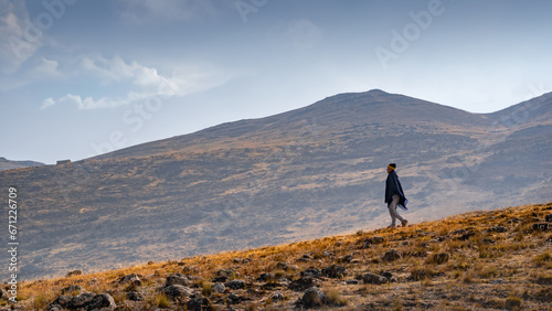 A man walking downhill wearing a black poncho in a lonely rocky and hazy landscape © Robaina Photograpahy