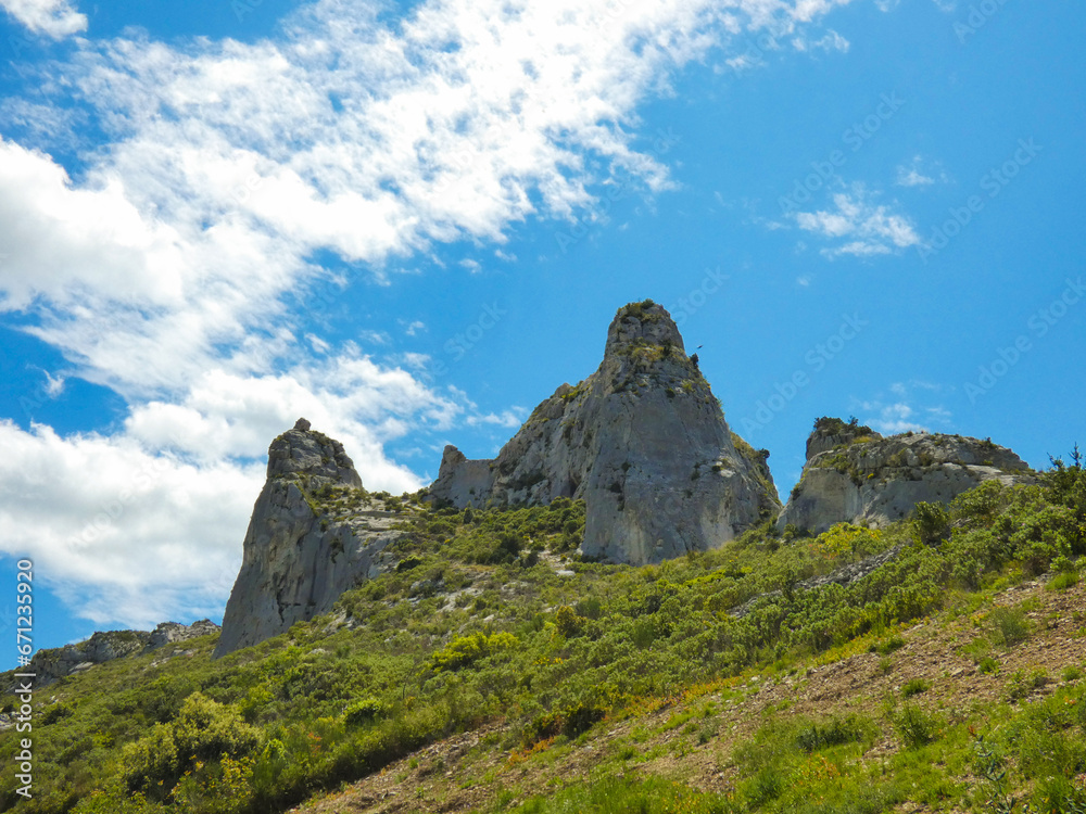 Fototapeta premium Wild landscape in the Alpilles in Provence in France with two rocky peaks.overlooking a hill covered in scrubland under blue sky dotted with white clouds