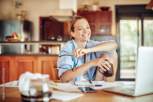 Happy young woman using her laptop in the kitchen at home
