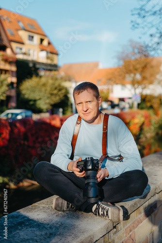 Man Sitting in Old European City And Holding Photo Camera. Contemporary Stylish Blogger And Photographer. Handsome man taking a selfie on a trip in Europe.