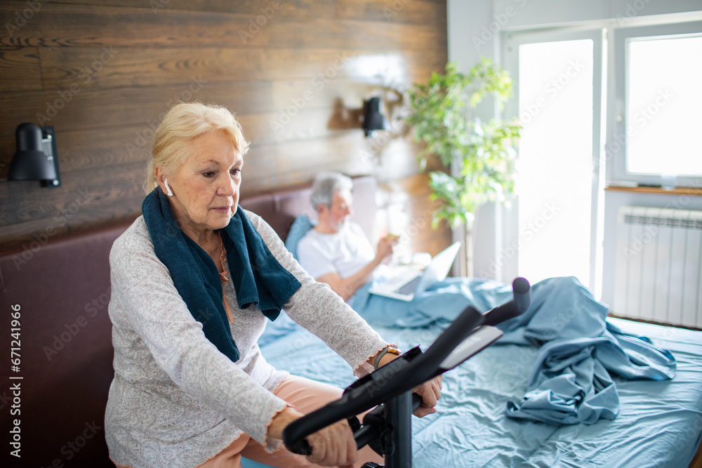 Senior woman exercising on a fitness bike in the bedroom at home Senior woman exercising on a fitness bike in the bedroom at home