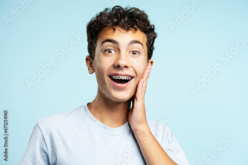 Excited handsome teenage boy wearing dental braces touching face looking at camera