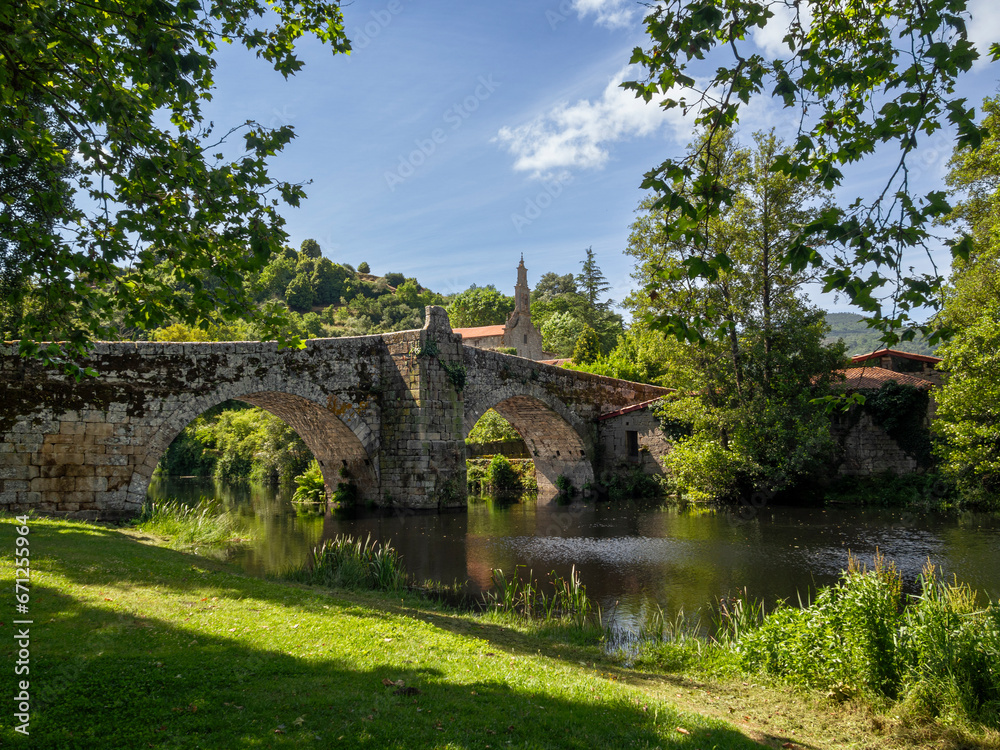 Puente antiguo romano de piedra con dos arcos en Allaritz pueblo de Orense provincia de Galicia España en verano de 2021, sobre el río con árboles de hojas verdes.