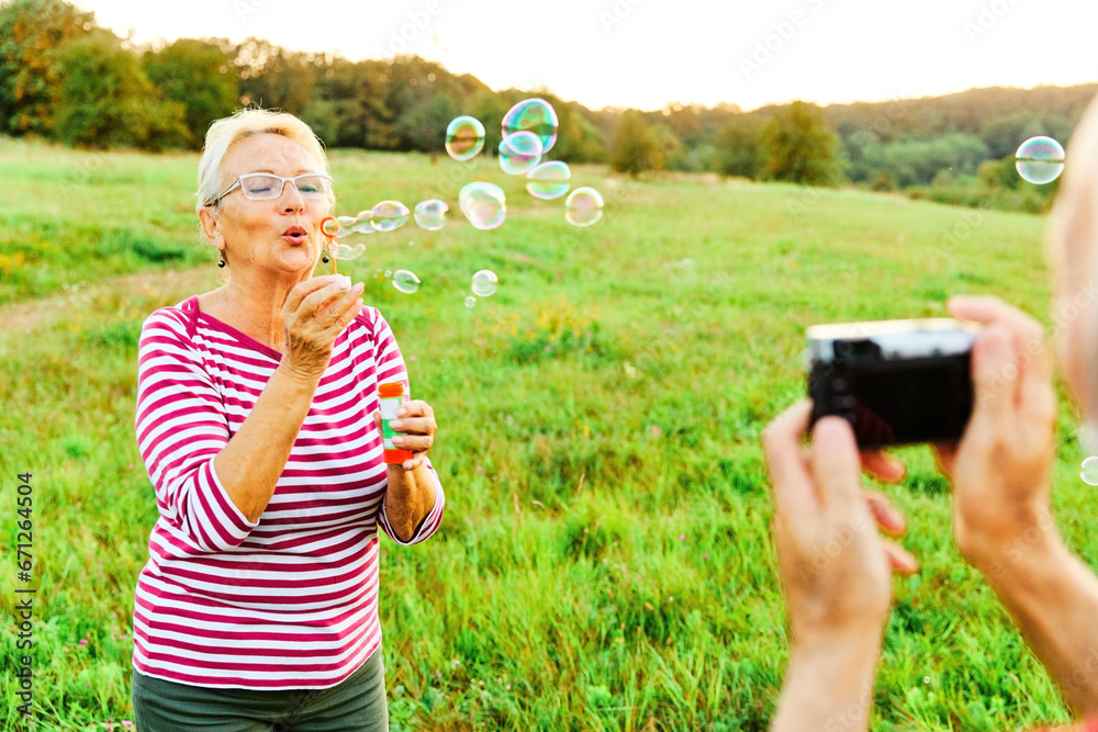 © Lumos sp - woman man outdoor senior couple happy fun retirement together bubble soap camera taking pictures blowing love old nature mature