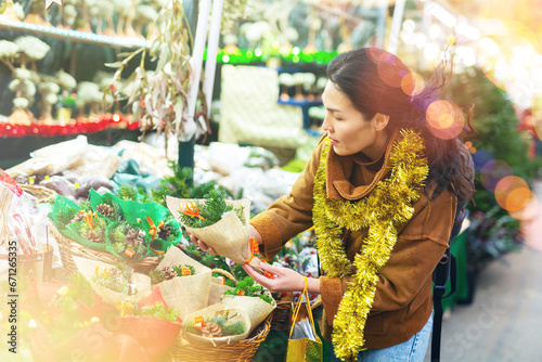 Portrait of positive asian woman choosing christmas souvenir bouquet at Xmas street fair