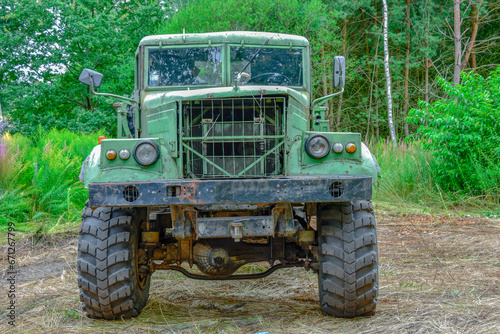 Stara, zdezelowana ciężarówka stojąca w sosnowym lesie. Karoseria kabiny jest koloru zielonego.