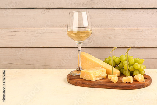 Wooden board with pieces of tasty Parmesan cheese, glass of wine and grapes on table