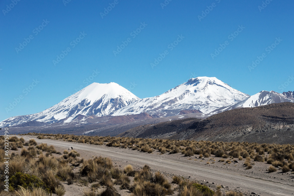 Image shows sand road and Parinacota and Pomerape volcano