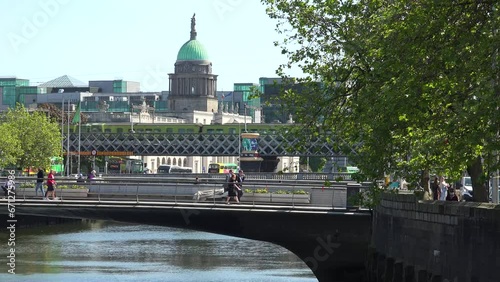 DUBLIN - JULY.27.2023 - People cross the Rosie Hackett Bridge over the River Liffey in Dublin, Ireland, passing the Custom House on a sunny day.