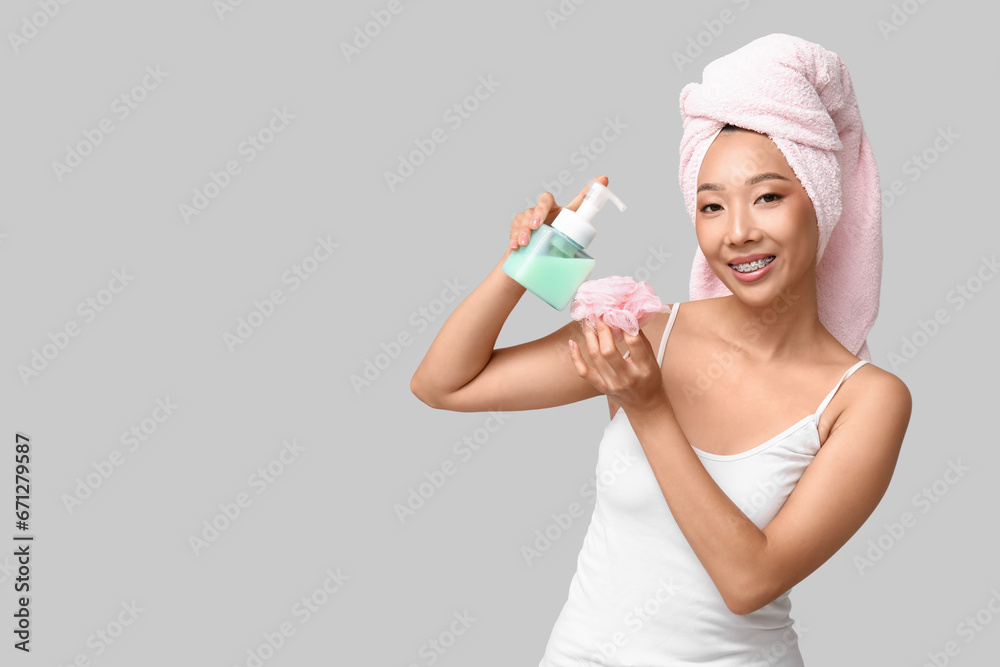 Young Asian woman with shower gel and loofah on light background Young Asian woman with shower gel and loofah on light background