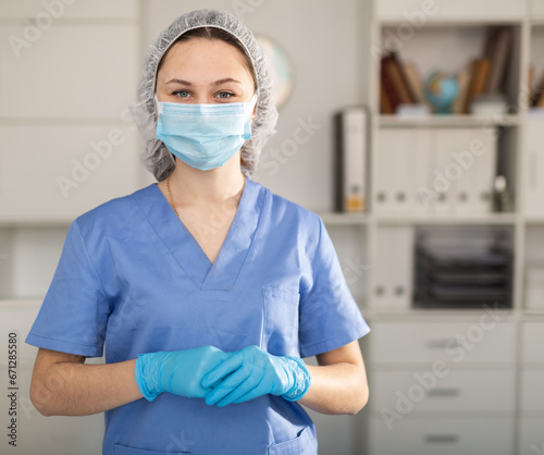 Masked girl nurse working in a hospital stands in resident s an office. Close-up portrait