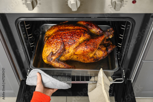 Woman taking tasty baked turkey from oven in kitchen. Thanksgiving Day celebration photo