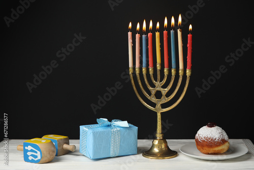 Menorah with candles, gift box and dreidels for Hanukkah on table against black background