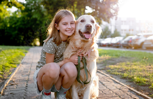 Cute preteen child girl hugging golden retriever dog at nature. Pretty kid petting purebred doggy pet labrador at park and smiling photo