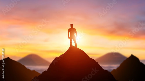 Silhouette of a business person on the top of a mountain peak in sunset background. Winner and conquer of businessman concept.