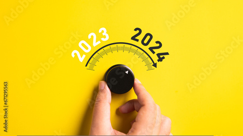 Close up of a hand adjusting volume button from year 2023 to 2024 on isolated yellow background. Happy New Year celebration concept. photo
