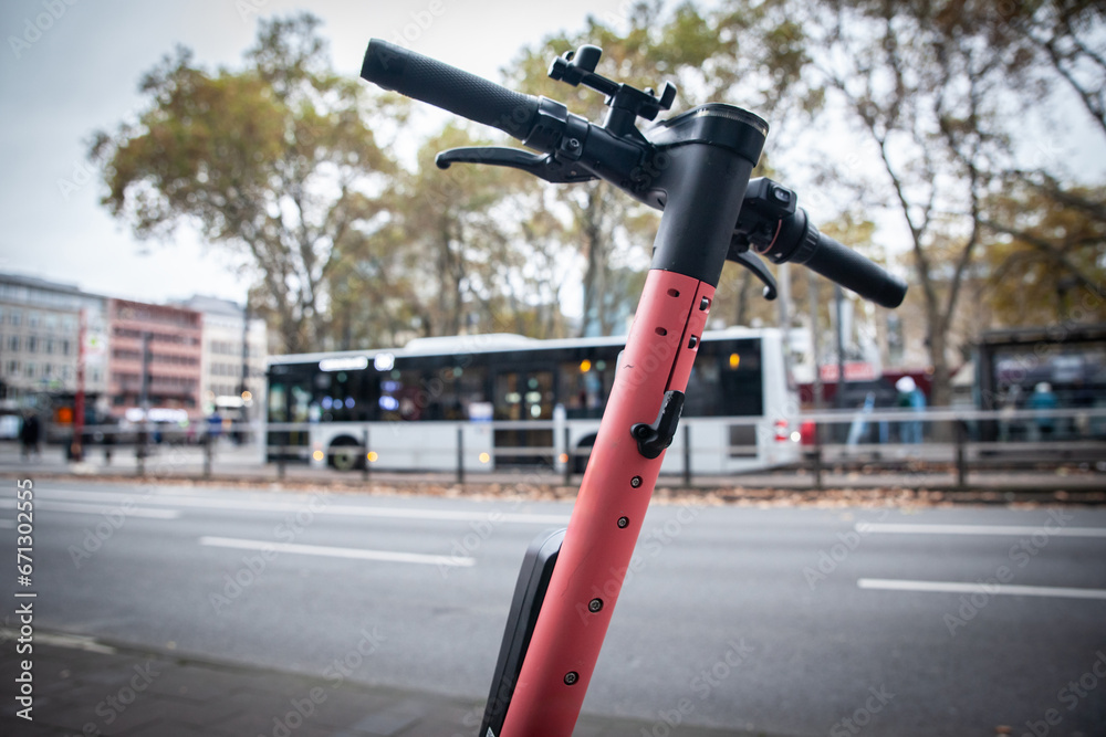 Fototapeta premium Selective blur on a pink electric scooter for rent, available in the streets of Cologne, Germany, in front of a bus of public transportation, belonging to a tech company specialized in vehicle sharing