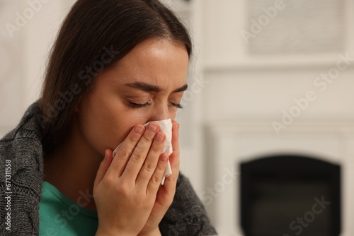 Sick woman wrapped in blanket with tissue blowing nose at home, closeup and space for text. Cold symptoms