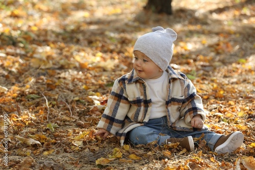 Cute little child on ground with dry autumn leaves outdoors  space for text