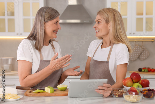 Happy mature mother and her daughter with tablet in kitchen
