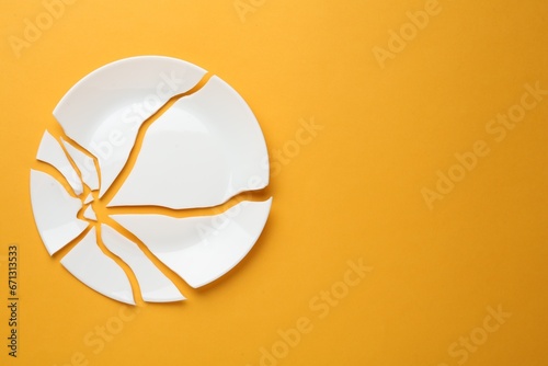 Pieces of broken ceramic plate on orange background, flat lay. Space for text photo