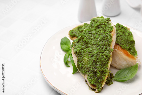 Delicious chicken breasts with pesto sauce and basil on white tiled table, closeup. Space for text