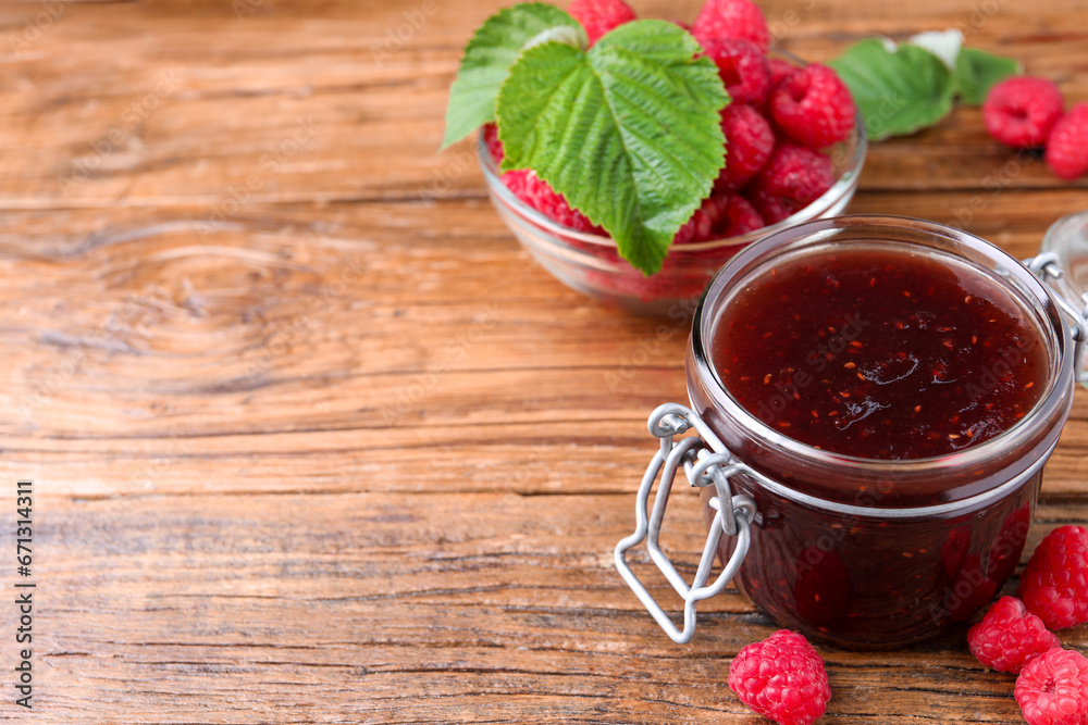 Jar of delicious raspberry jam, fresh berries and green leaves on wooden table. Space for text Jar of delicious raspberry jam, fresh berries and green leaves on wooden table. Space for text