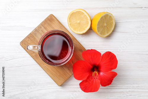 Delicious hibiscus tea, halves of lemon and beautiful flower on white wooden table, flat lay