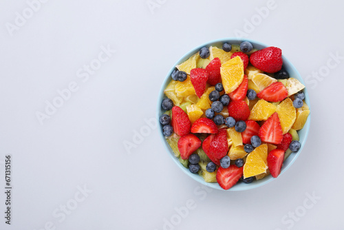 Yummy fruit salad in bowl on light grey background  top view. Space for text