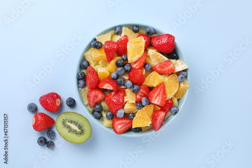 Yummy fruit salad in bowl and ingredients on light blue background  flat lay