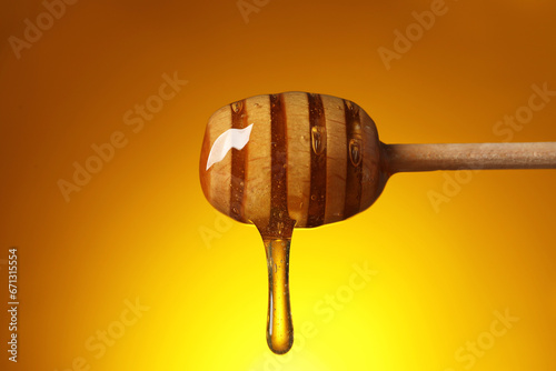 Pouring honey from dipper against golden background, closeup