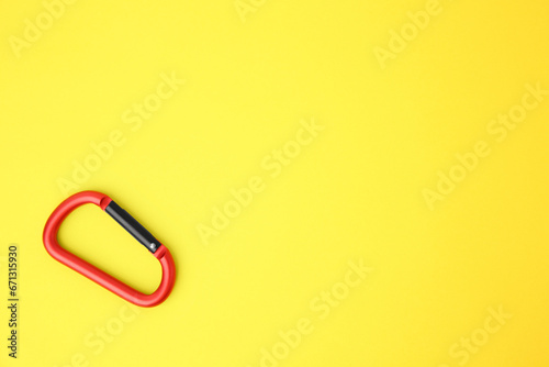 One red carabiner on yellow background, top view. Space for text