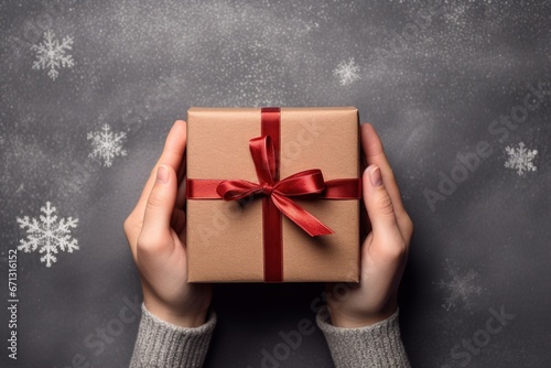 Close-up, top view of a woman's hand holding a box of the day for Christmas on a cement floor backdrop with white snowflakes.