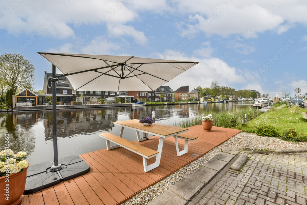 an outdoor area with tables and umbrellas on the side of the water in front of a row of houses
