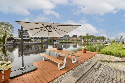 an outdoor area with tables and umbrellas on the side of the water in front of a row of houses