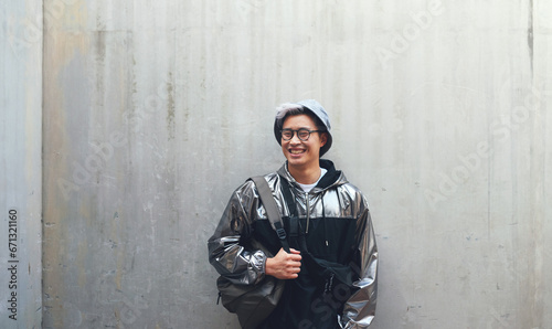 Fashion, student and gen z asian male happy, confident and . with cool clothes on wall background, smile and chilling. Travel, fashionable and Japanese guy outdoors casual, contemporary and stylish photo
