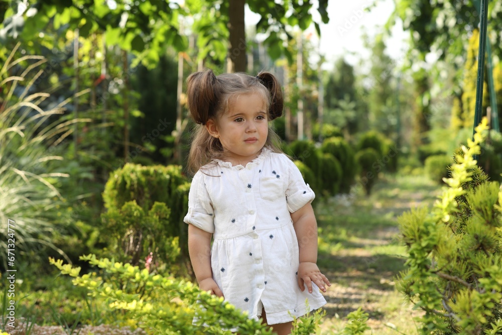 Cute little girl walking near green plants in park Cute little girl walking near green plants in park