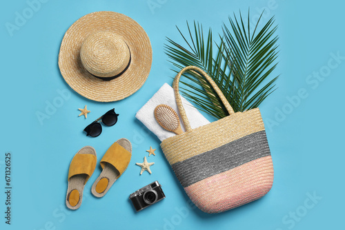 Wicker bag, camera, palm leaves and beach accessories on light blue background, flat lay