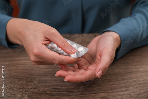 Woman taking antidepressant pill out from blister at wooden table, closeup