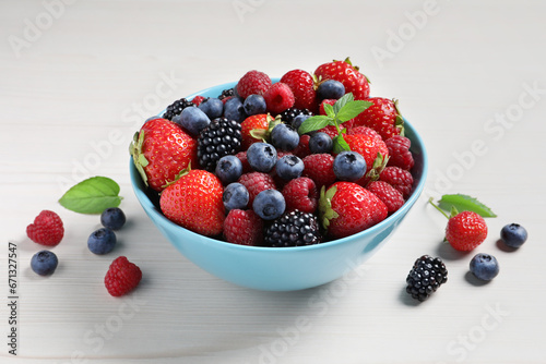 Many different fresh ripe berries in bowl on white wooden table