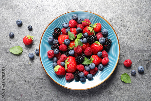 Many different fresh ripe berries in plate on grey table, flat lay