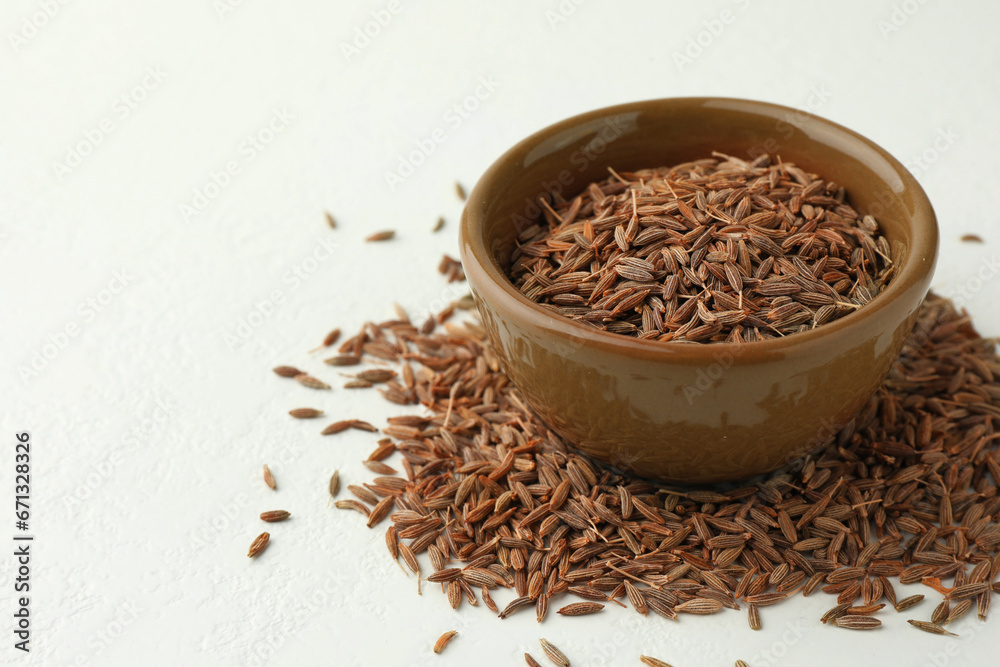 Caraway (Persian cumin) seeds and bowl on white table, space for text Caraway (Persian cumin) seeds and bowl on white table, space for text