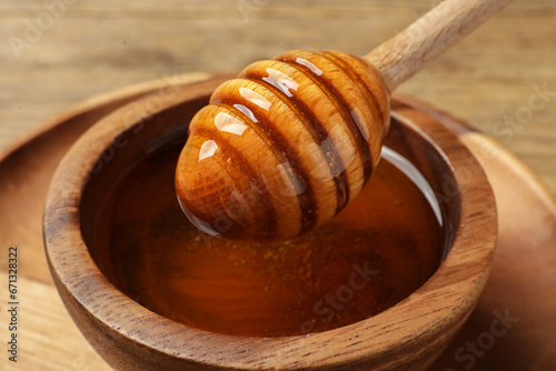 Dipper with honey in wooden bowl at table, closeup