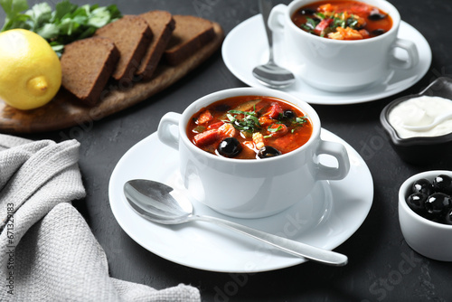 Meat solyanka soup with sausages and olives served on dark grey textured table