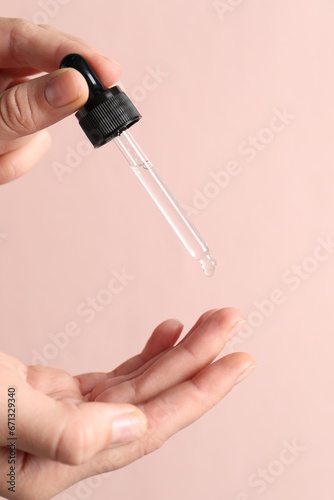 Woman applying cosmetic serum onto fingers on light pink background  closeup
