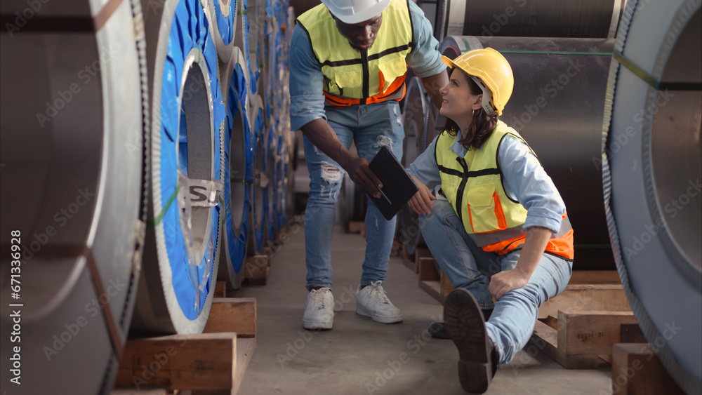 A male factory worker assists a female industrial worker who has an injured leg. As a result of working with hefty and huge objects A male factory worker assists a female industrial worker who has an injured leg. As a result of working with hefty and huge objects