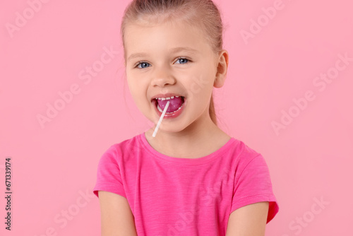 Cute little girl eating lollipop on pink background